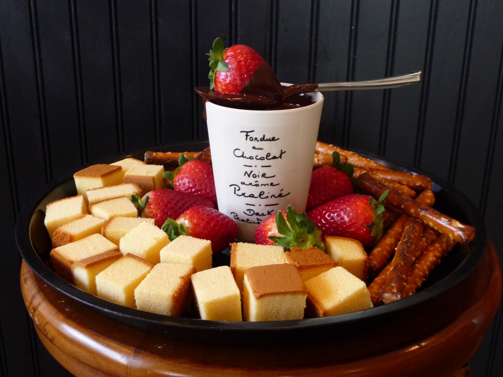 white ceramic mug on top sppon and strawberry surrounded leche plan and strawberry on black round shape tray