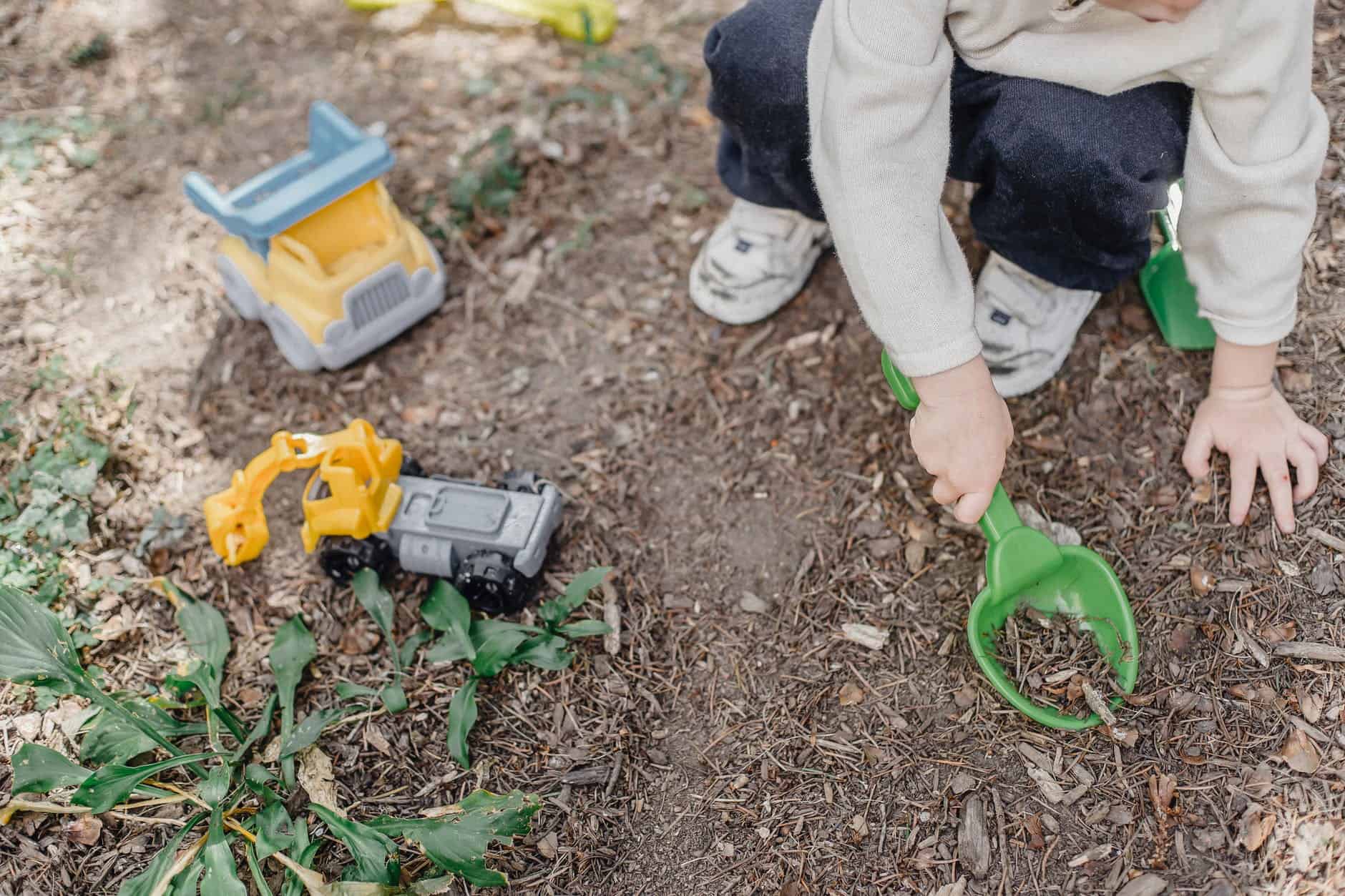 little kid playing with plastic shovel in yard