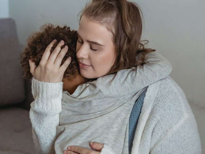 loving mother comforting crying son on couch